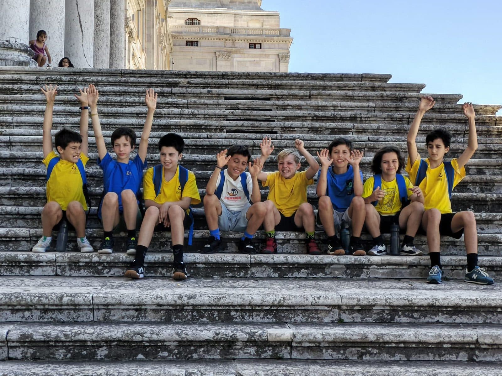 Jovens atletas do Camões Andebol de braços no ar, sentados numa escadaria